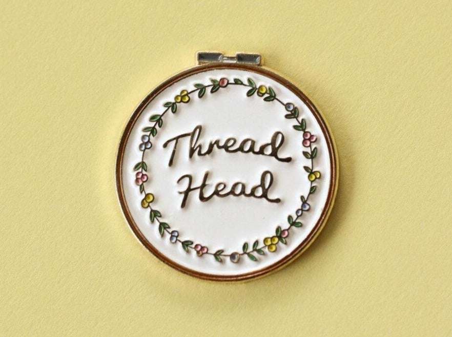 A metal circle reading 'Thread Head' in the centre surrounded by a floral design. Background is pastel yellow