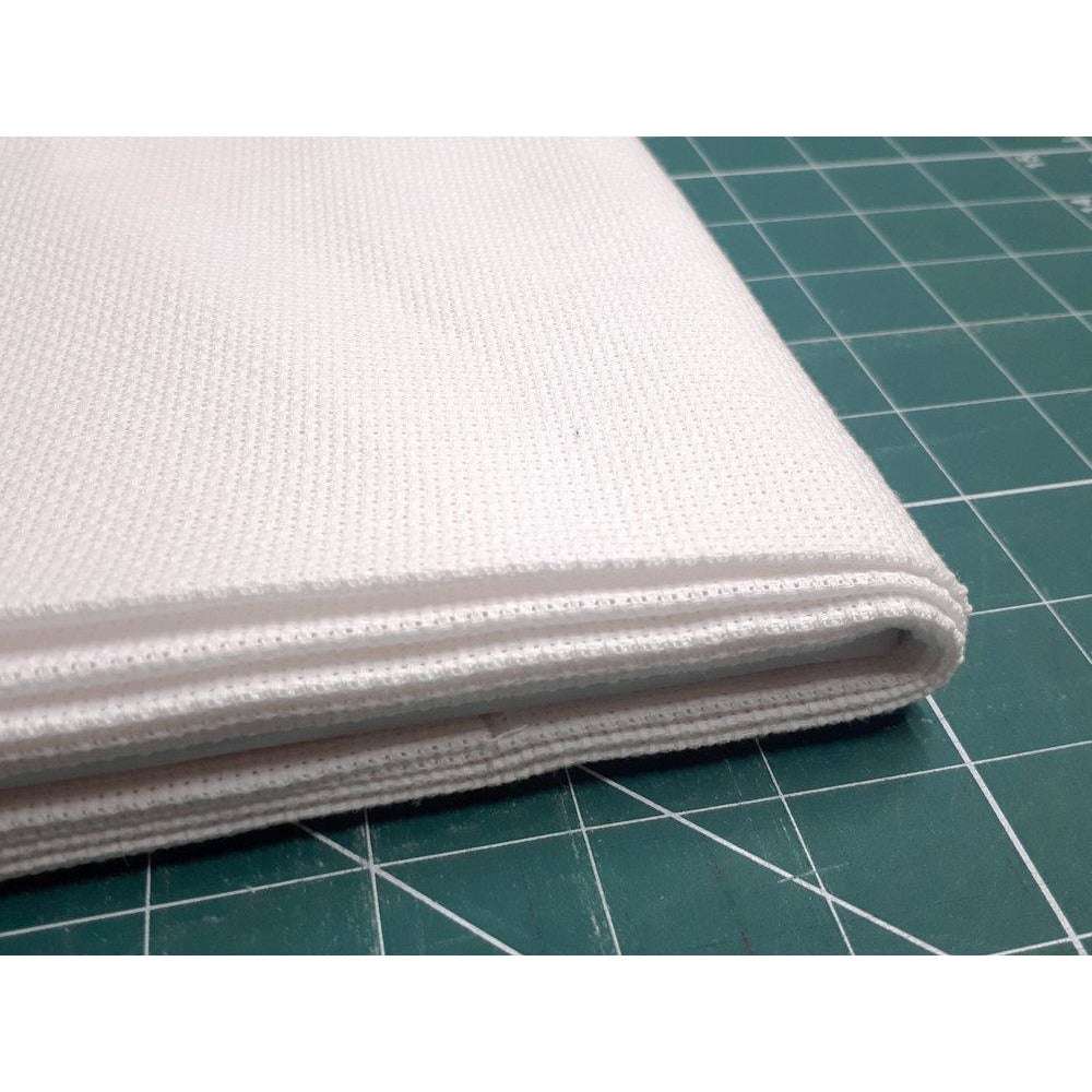 A stack of white aida cross stitch fabric lies on a green measuring board