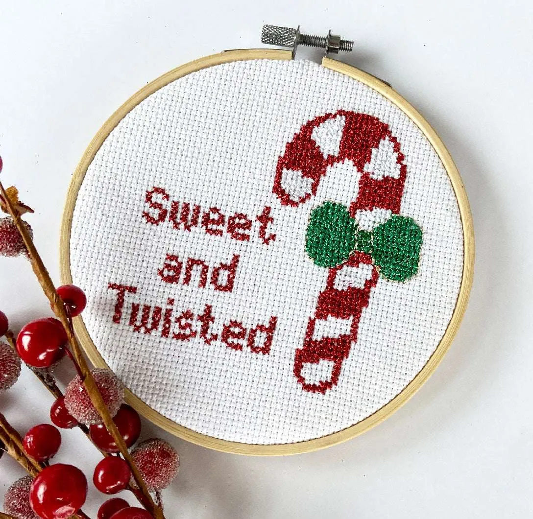 Cross stitch of a red and white candy cane with a green bow with the text 'Sweet and twisted' next to do it in red text