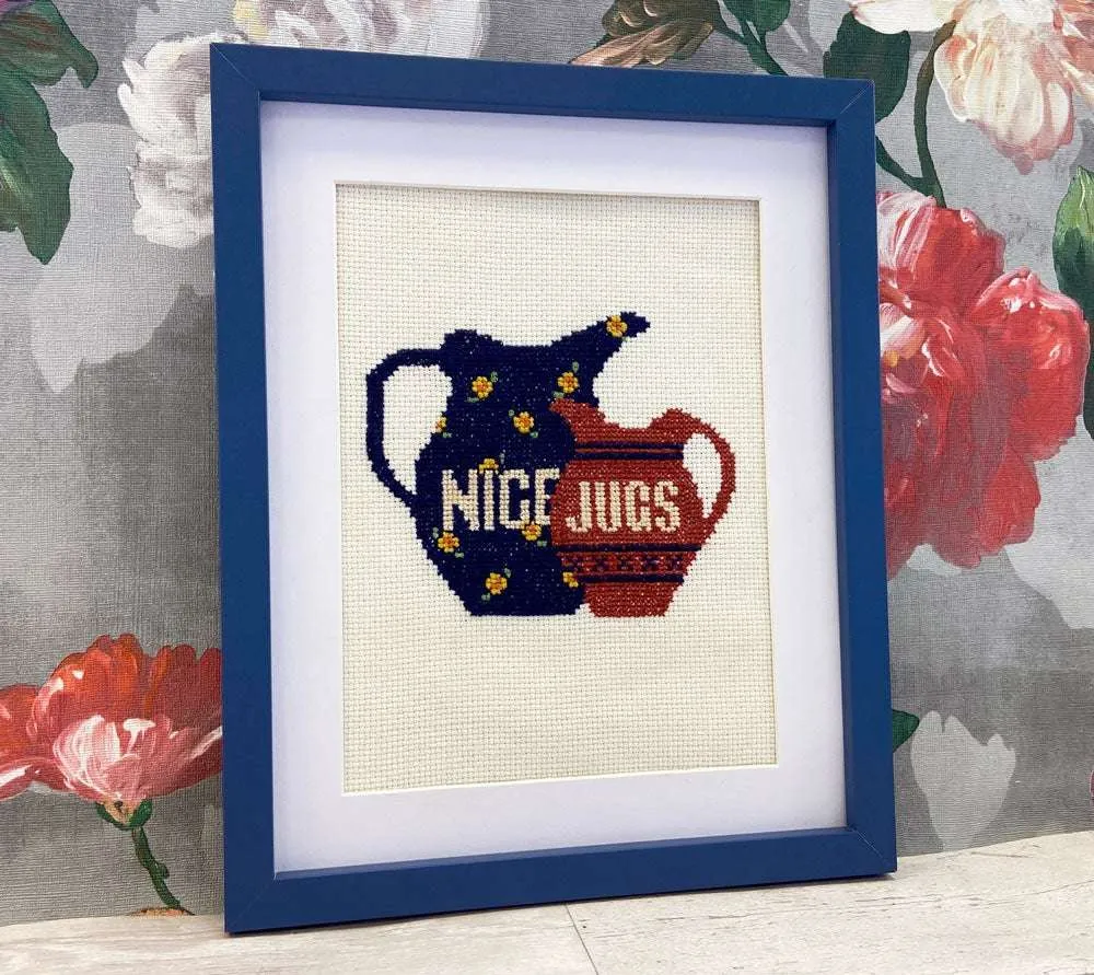 A framed cross stitch of two jugs that reads across one 'NICE' and the other 'JUGS'.