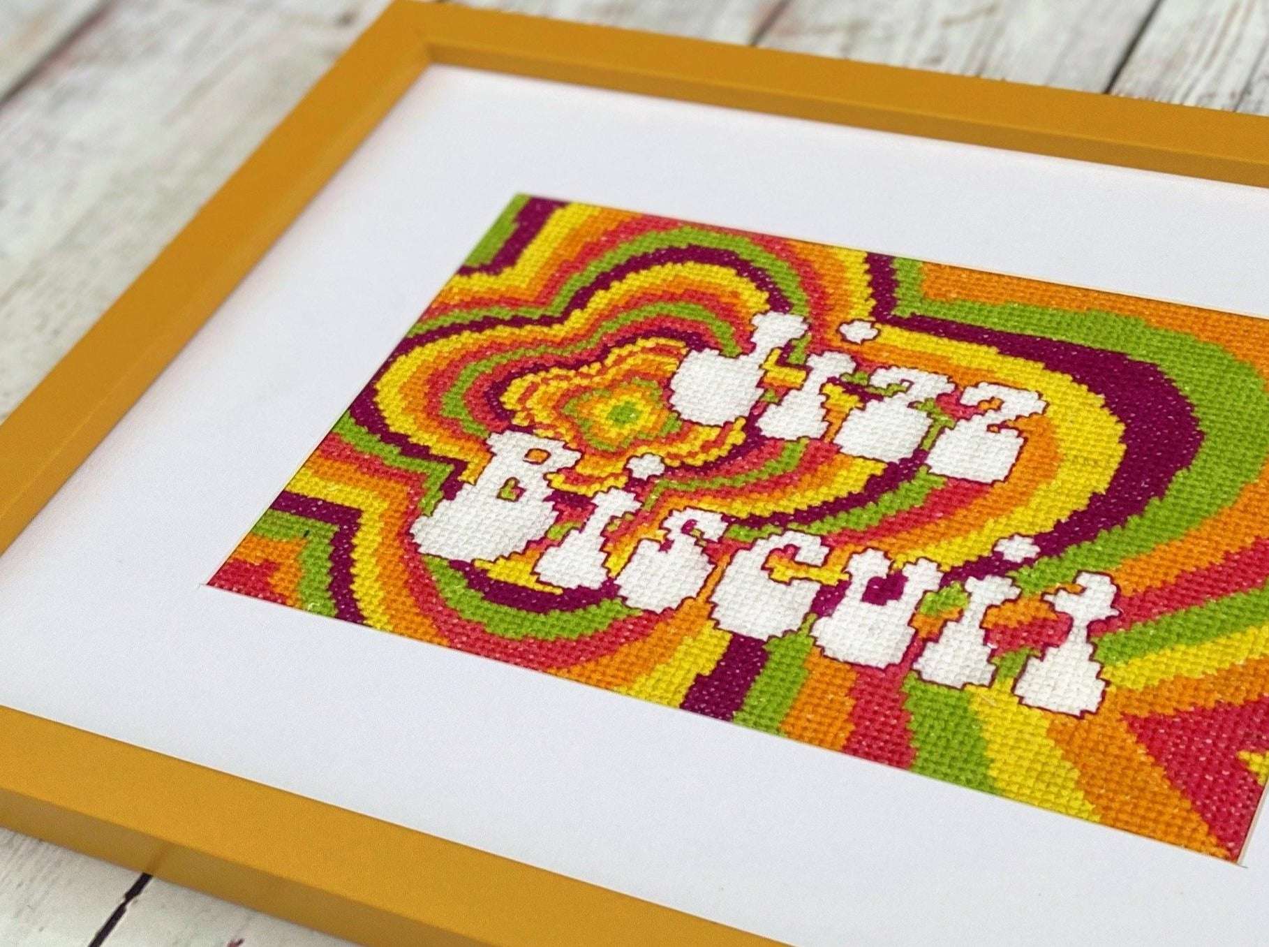 a colourful, psychedelic patterned cross stitch featuring bright colours and the words jizz biscuit written in a retro 1970s font