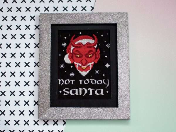 Cross stitch design of Satan wearing a santa had. Below it are the words not today satan. it is mounted in a silver glittery picture frame