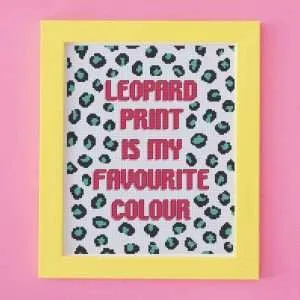Cross stitch design with brightly coloured leopard print. The words leopard print is my favourite colour is stitched in bright pink. It is framed in a yellow picture frame