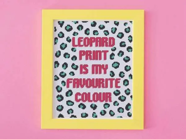 Cross stitch design with brightly coloured leopard print. The words leopard print is my favourite colour is stitched in bright pink. It is framed in a yellow picture frame